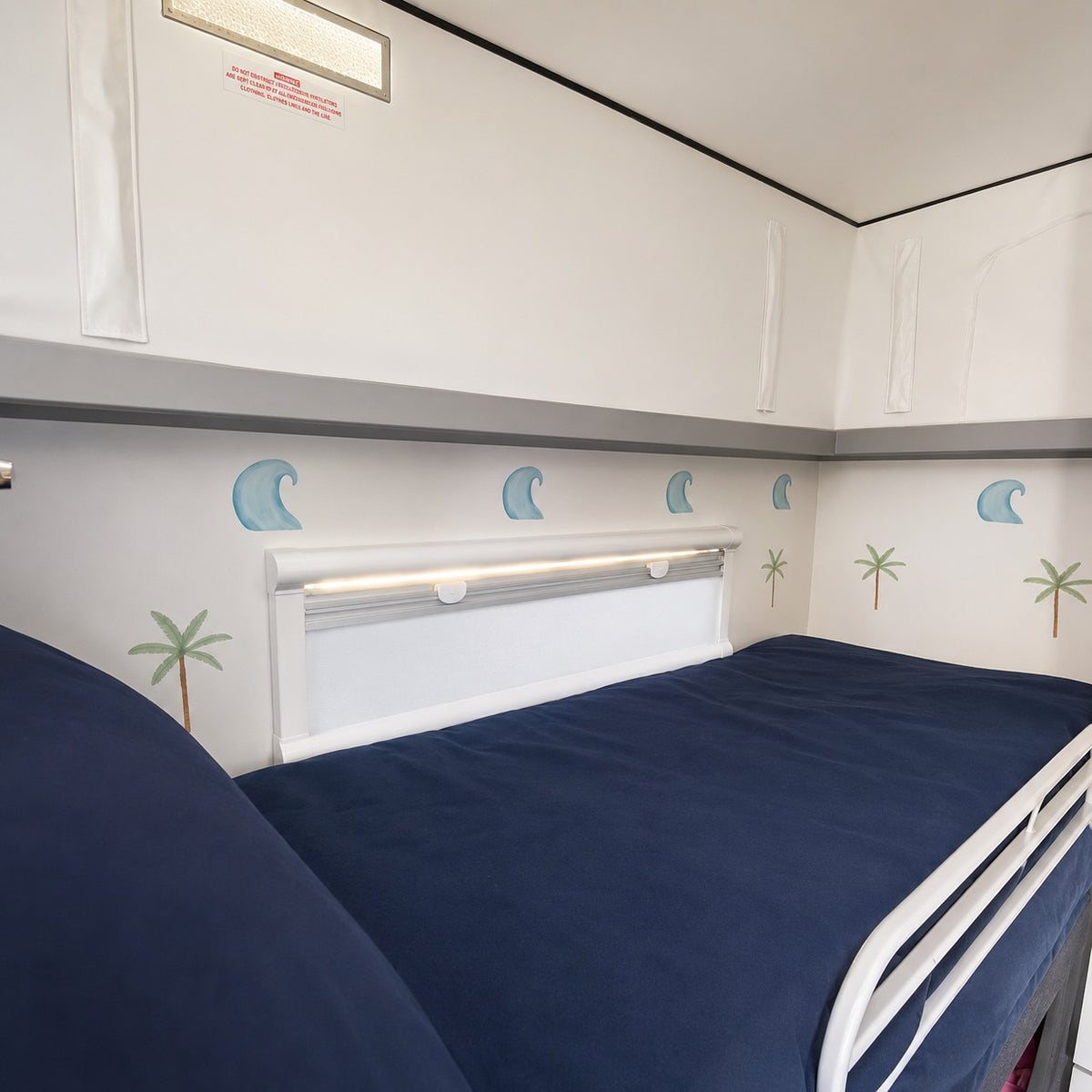 A twin bunk bed with navy blue bedding in the top bunk, featuring palm tree and wave decals on the wall.